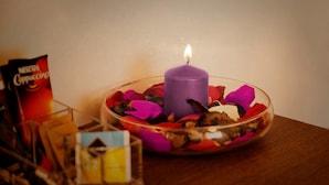 A purple candle in a glass bowl with rose petals and dried flowers on a wooden table. - B&B Sul Corso (Salerno)