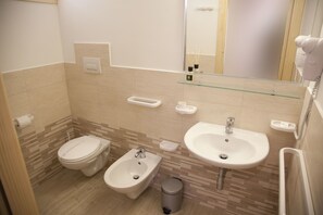 A modern bathroom with a toilet, bidet, sink, and mirror.