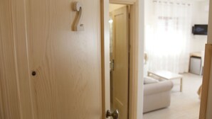 Une porte en bois portant le numéro 2, qui donne sur une pièce où se trouvent un canapé blanc et un téléviseur fixé au mur.