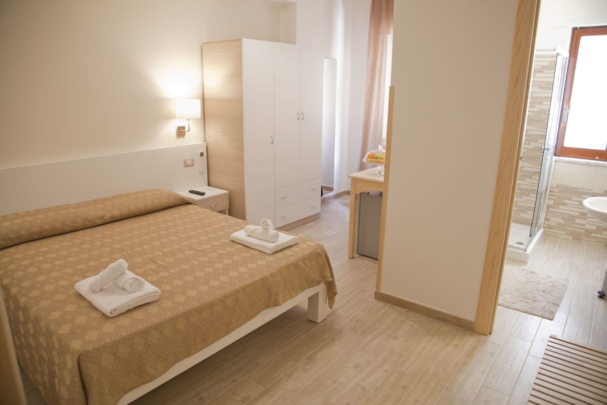 A hotel room with a bed, a desk, a wardrobe, and a bathroom visible through an open door.