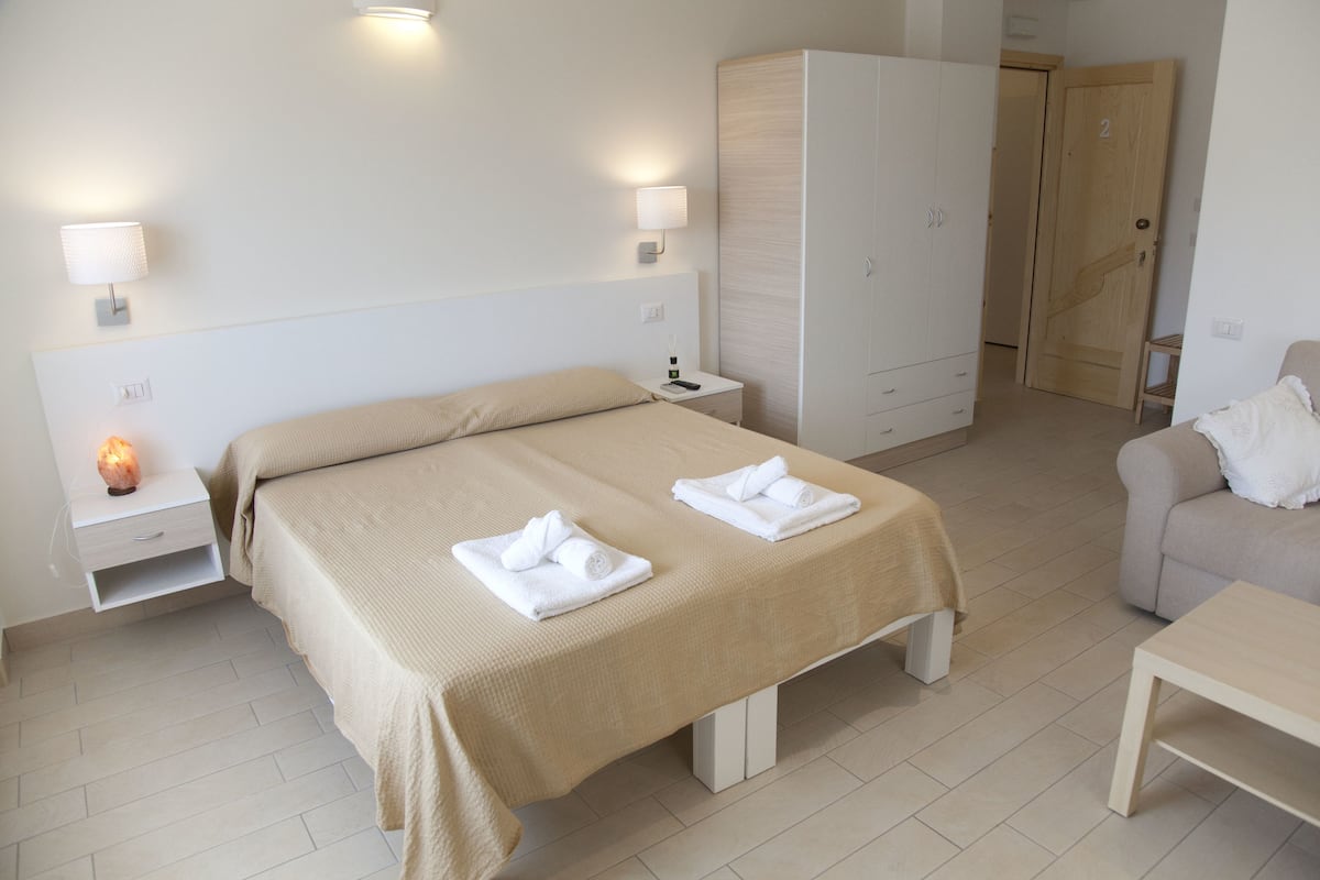 A hotel room with a bed, bedside tables, a wardrobe, and a seating area.