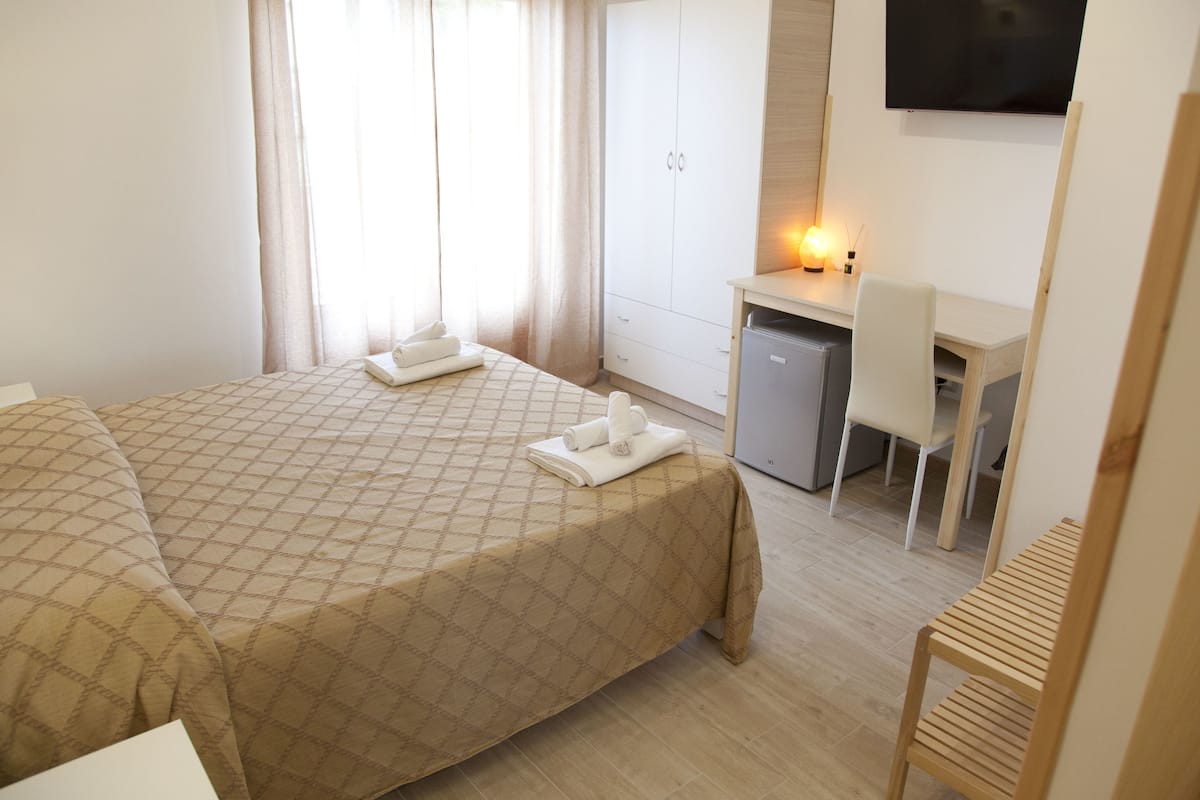 A hotel room with a bed, a desk, a chair, and a wardrobe.