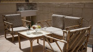 Un coin salon extérieur aménagé avec des meubles en osier, comprenant une table pour deux personnes, un panier de fruits et des verres.
