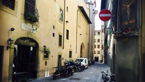 Une rue étroite, bordée de motos garées et d’une voiture blanche, un panneau d’interdiction d’accès et un bâtiment sur lequel on peut lire l’inscription « Piazza ».
