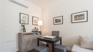 Un espace de vie compact comprenant un coin cuisine, une table à manger avec deux chaises, un canapé et des tableaux encadrés accrochés aux murs.