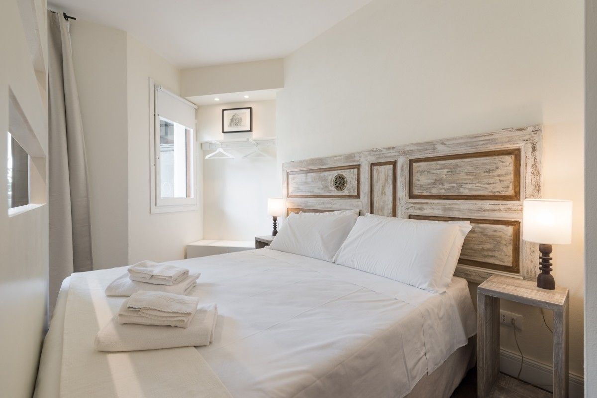 A neatly made bed with folded towels, a rustic headboard, a bedside lamp, and a framed picture on the wall.