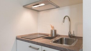 Une cuisine compacte dotée d’un évier en acier inoxydable, d’une cuisinière intégrée et d’une hotte aspirante.