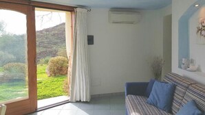 A room with a sliding glass door leading to a garden, a sofa, and an air conditioning unit on the wall. - Villa Ludduì L2 (Budoni)