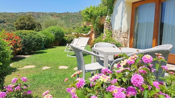 A garden with wicker furniture, a stone wall, and flowering plants. - Villa Ludduì L2 (Budoni)
