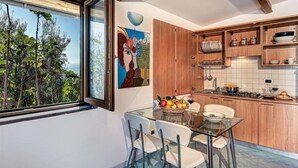 A modern kitchen with wooden cabinets, a dining table with chairs, and a view of the outdoors. - The Muse (Massa Lubrense)
