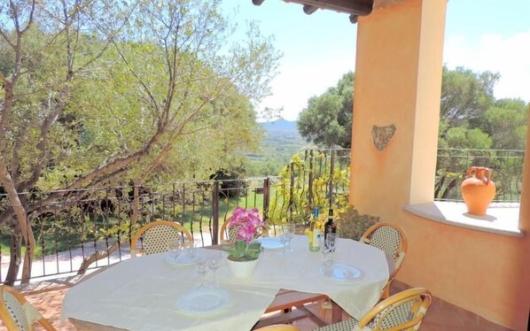 An outdoor dining area with a table set for two, surrounded by wicker chairs.