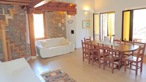 A cozy room with a wooden dining table and chairs, a white sofa, and a stone wall. - Villa Ludduì L (Budoni)