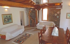 Relax in this inviting space with a dining table, sofa, and bench, surrounded by exposed beams and a stone wall.