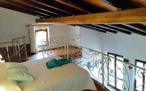 Une chambre avec un lit, un balcon doté d’une rambarde en métal et une poutre en bois au plafond.