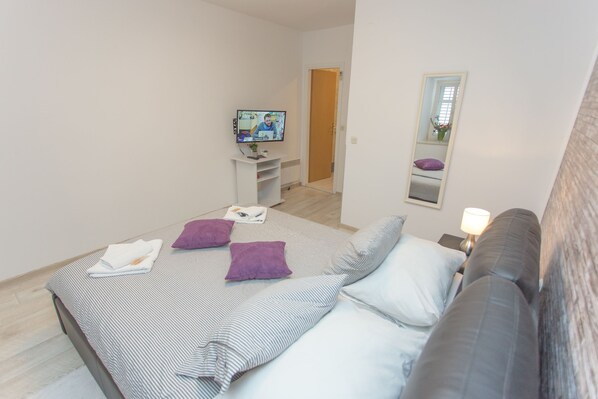 Un dormitorio con cama, televisor, sofá y espejo.