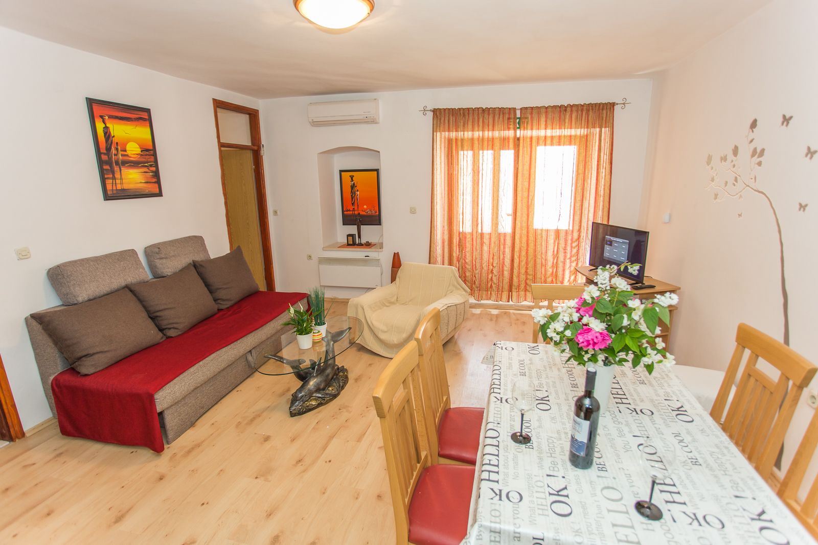 A living room with a sofa, a dining table with chairs, a TV, and a window with curtains.