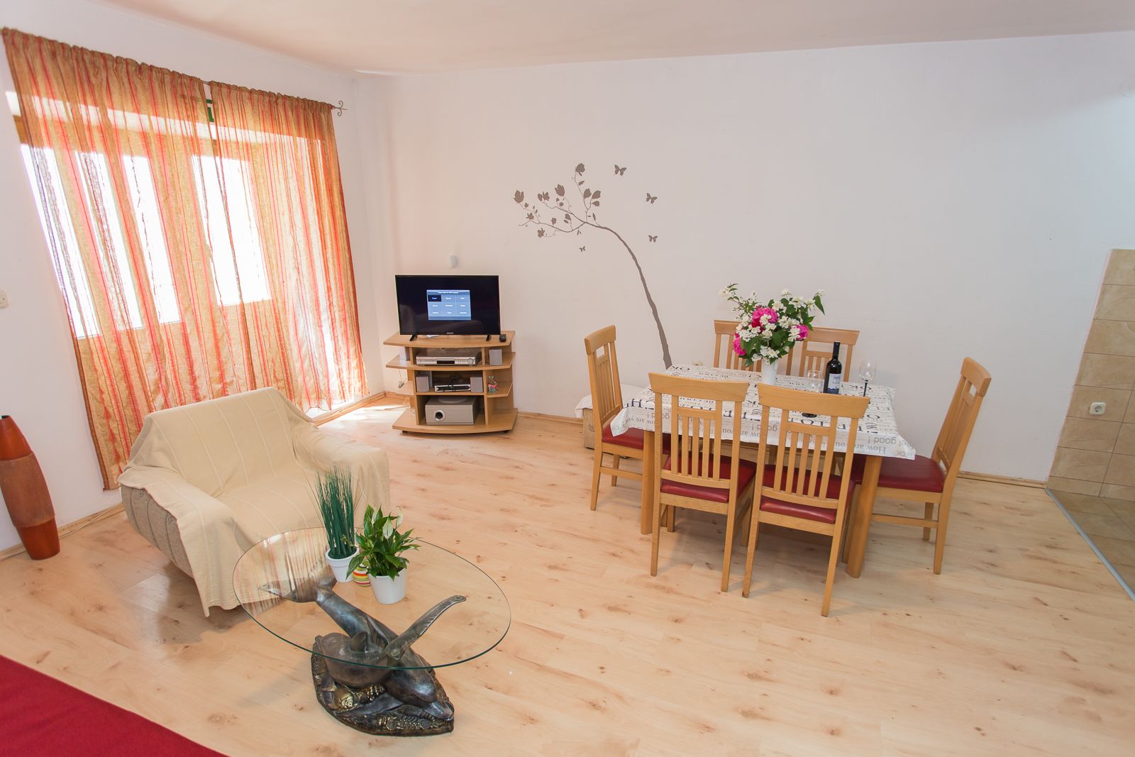 A living room with a TV, a dining table with chairs, a sofa, and a decorative fish sculpture on a glass table.