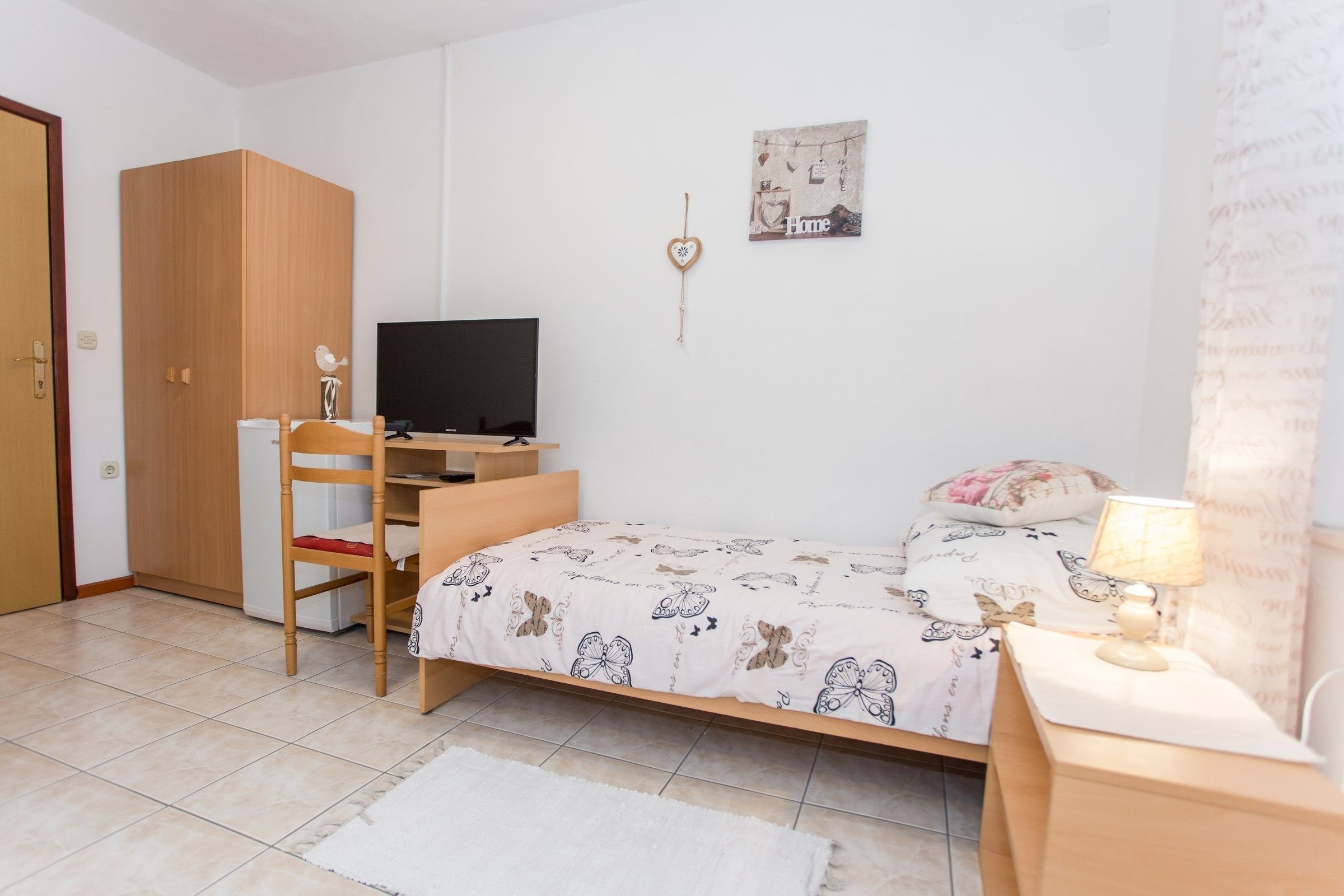 Un dormitorio con cama, escritorio con computadora, silla, armario, televisor y decoración en la pared.