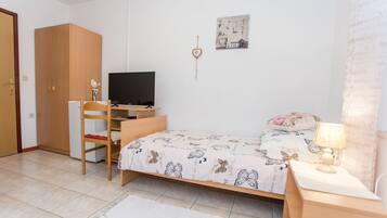 Un dormitorio con cama, escritorio con computadora, silla, armario, televisor y decoración en la pared.