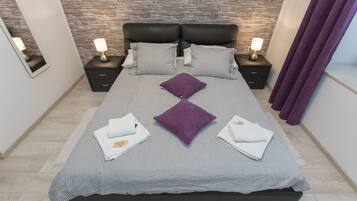Une chambre moderne avec une tête de lit à motifs de briques, un grand lit avec une literie à rayures et deux coussins violets, deux tables de chevet avec des lampes et un rideau violet.
