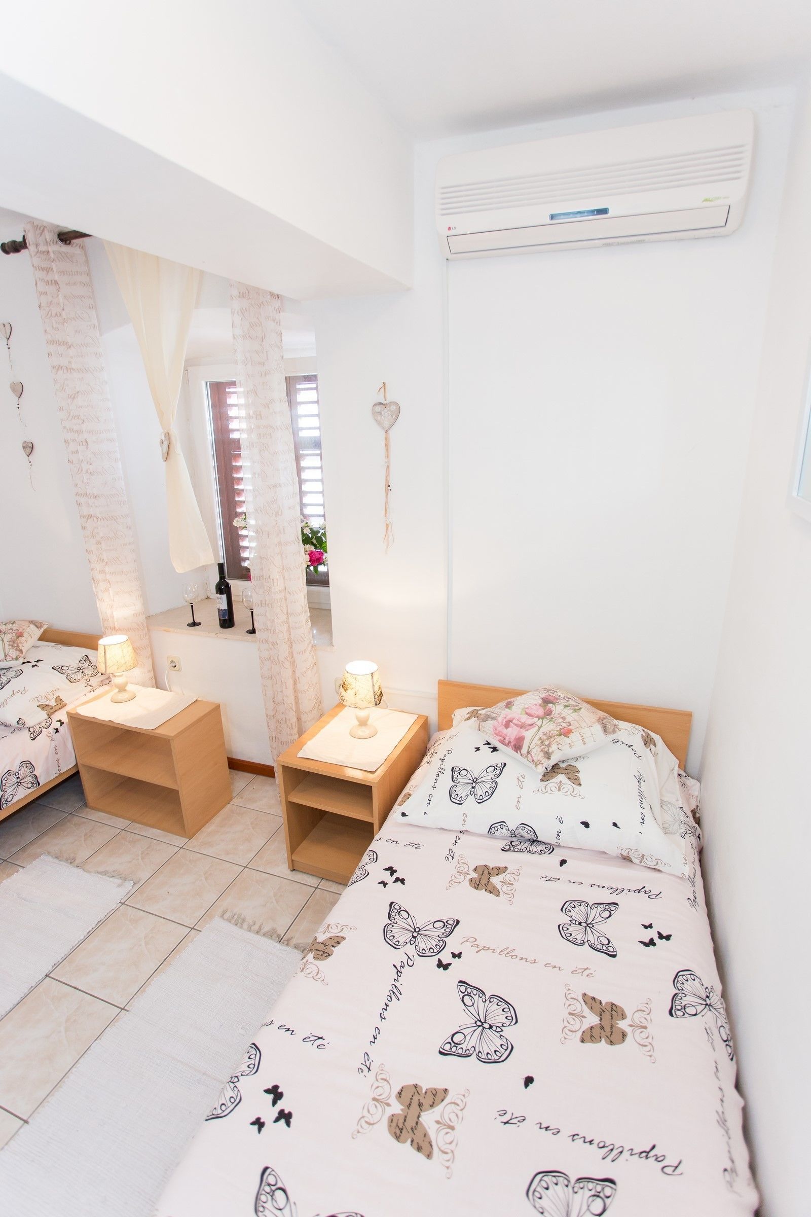 Un dormitorio con dos camas, una ventana con cortinas, un espejo, una mesita de noche con lámpara y un equipo de aire acondicionado.