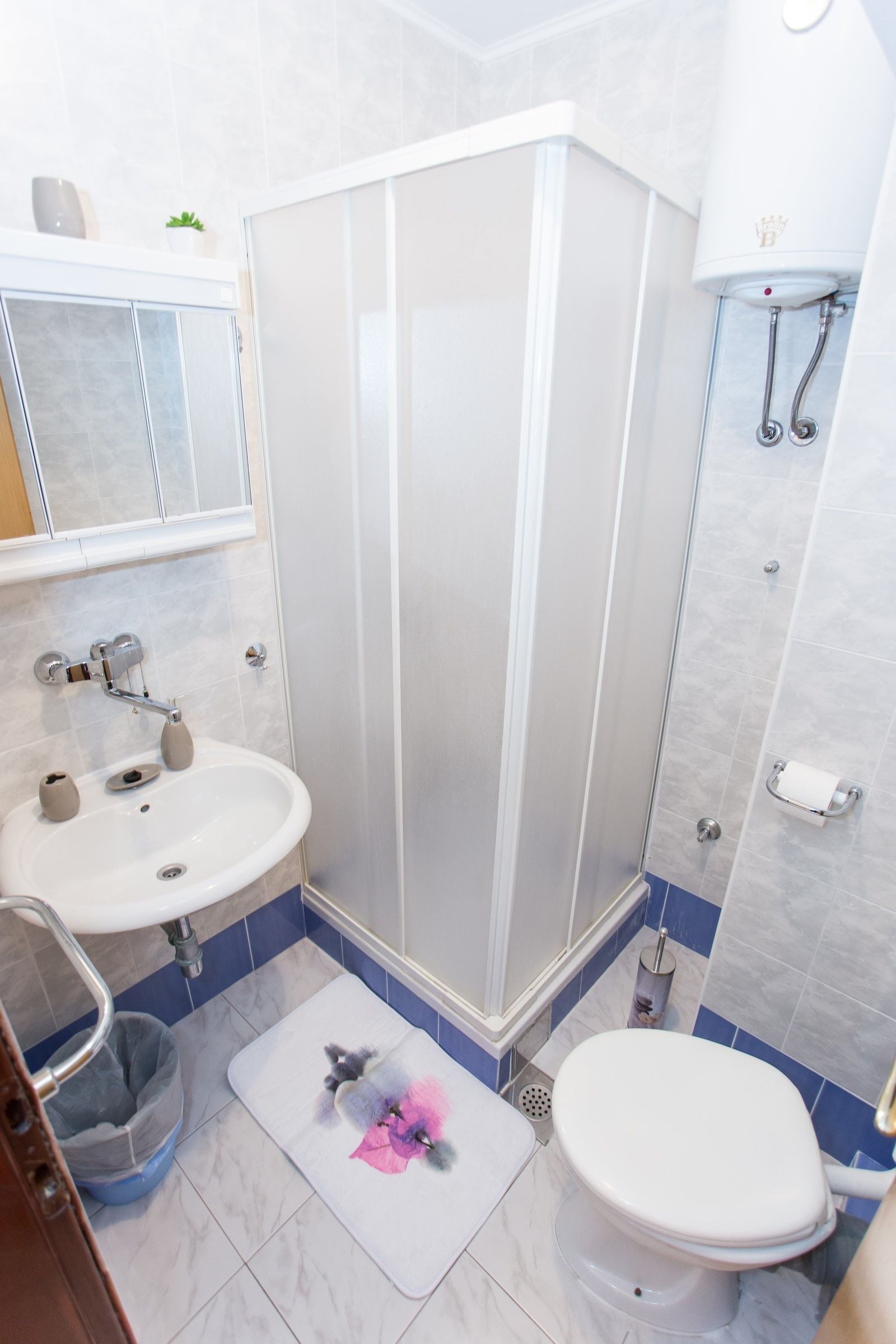 A bathroom with a shower, sink, toilet, and a small trash bin.