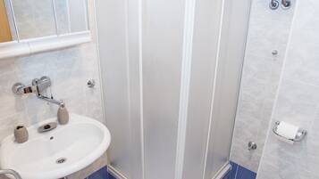 A bathroom with a shower, sink, toilet, and a small trash bin.