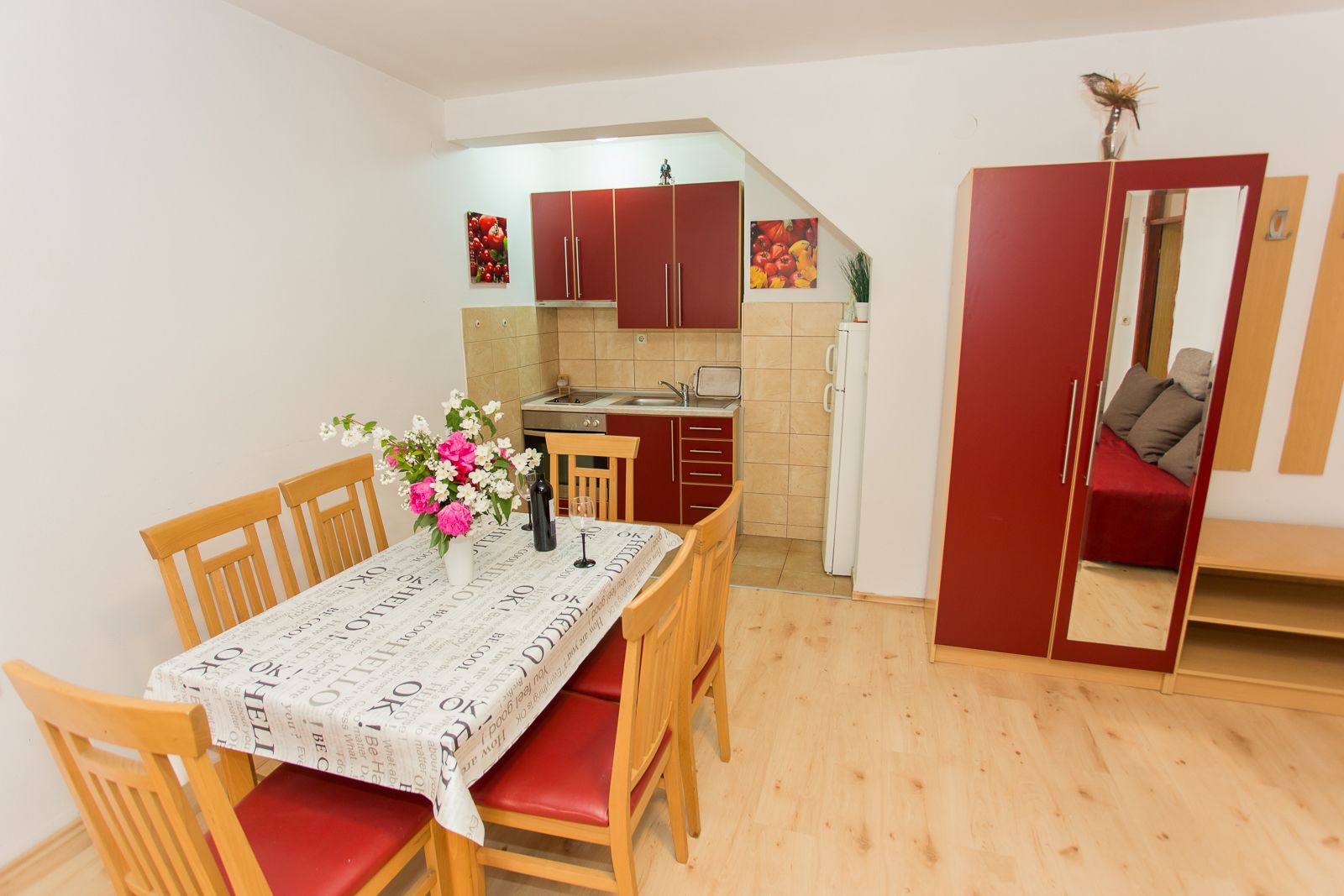 A compact kitchen with wooden cabinets, a dining table with a red tablecloth, and a small refrigerator.