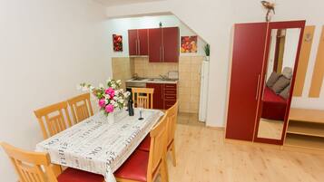 A compact kitchen with wooden cabinets, a dining table with a red tablecloth, and a small refrigerator.