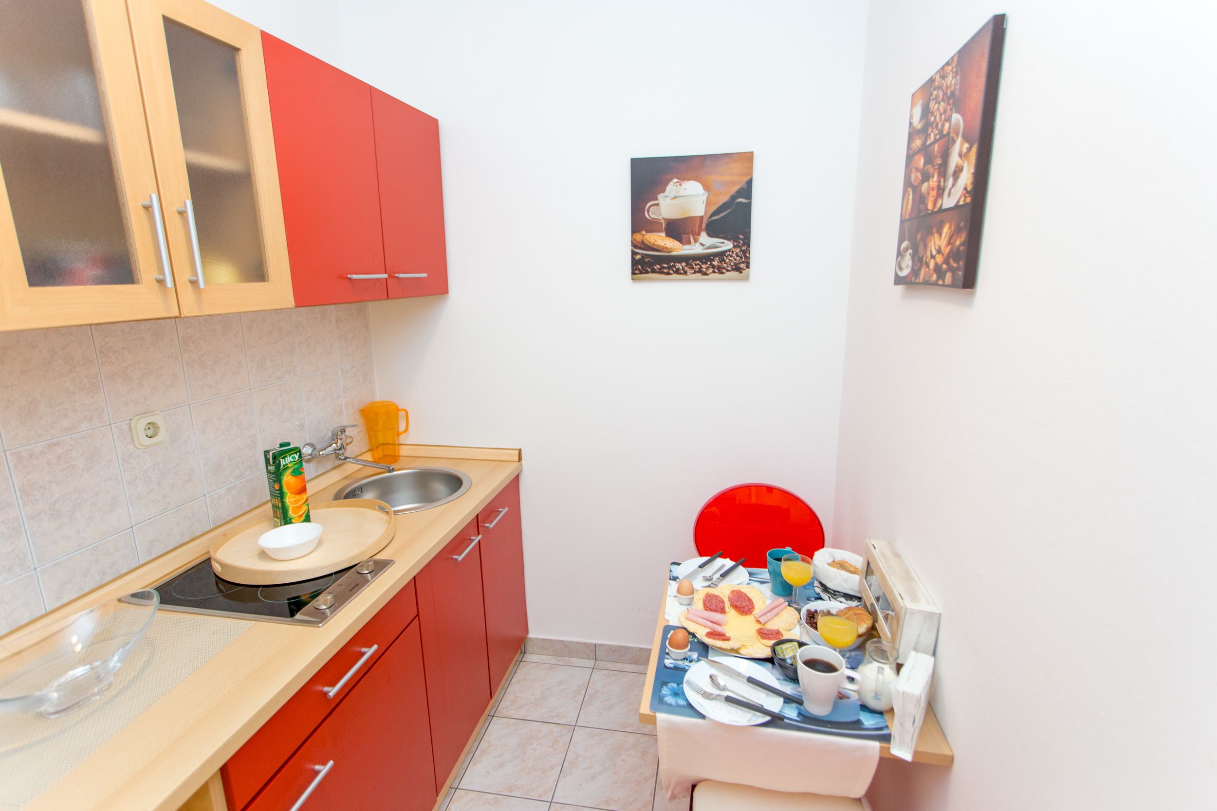Una cocina compacta con un mueble rojo, un lavabo y una zona de comedor con una silla roja.