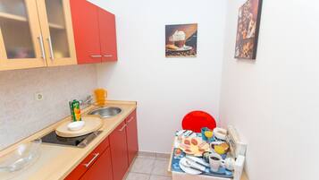 Una cocina compacta con un mueble rojo, un lavabo y una zona de comedor con una silla roja.