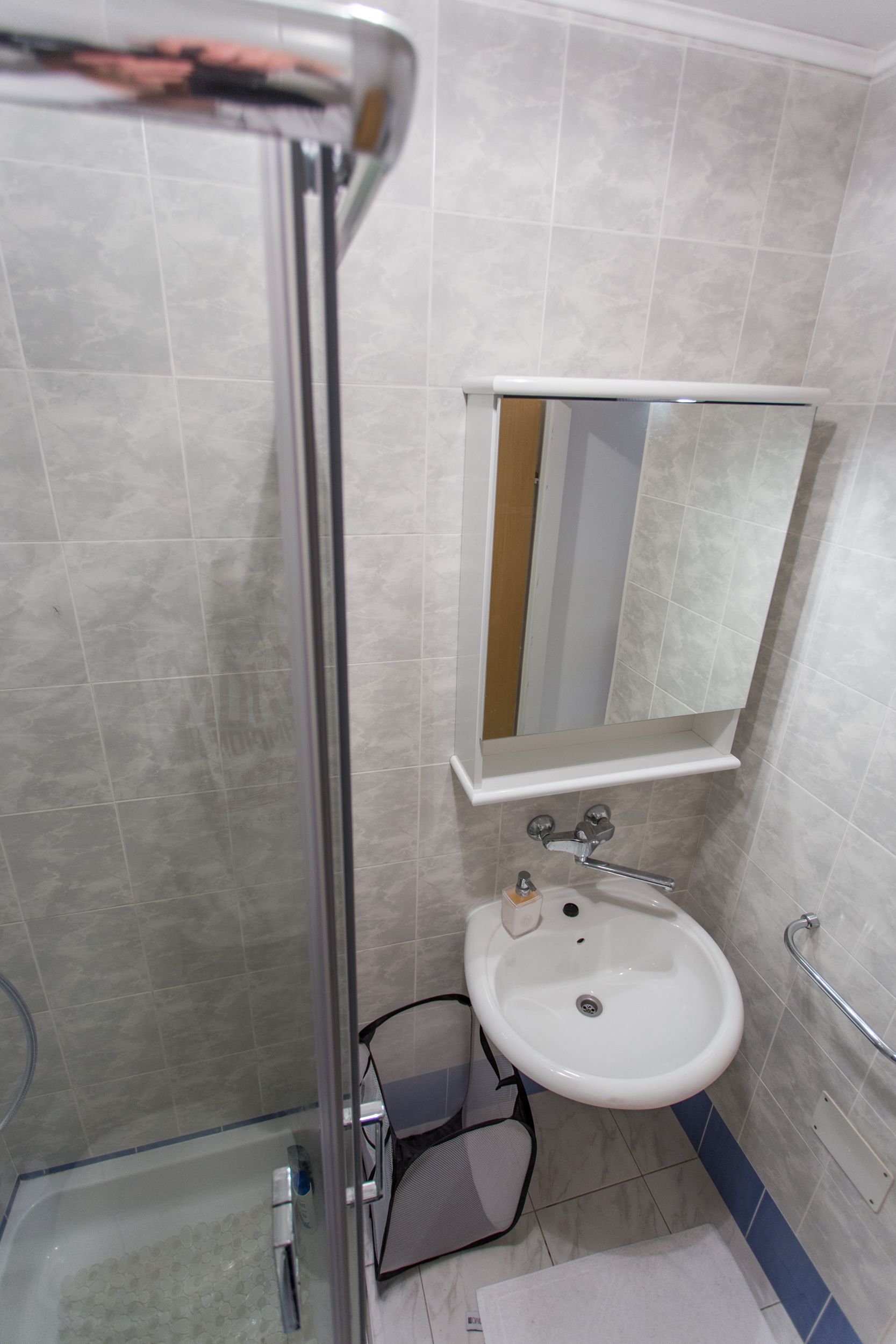 A bathroom with a glass shower enclosure, a white sink with a mirror above it, and a blue-tiled floor.