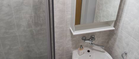 A bathroom with a glass shower enclosure, a white sink with a mirror above it, and a blue-tiled floor.