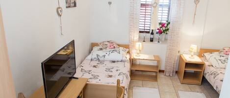 A compact bedroom with a bed, a desk, a chair, a TV, and a small refrigerator.