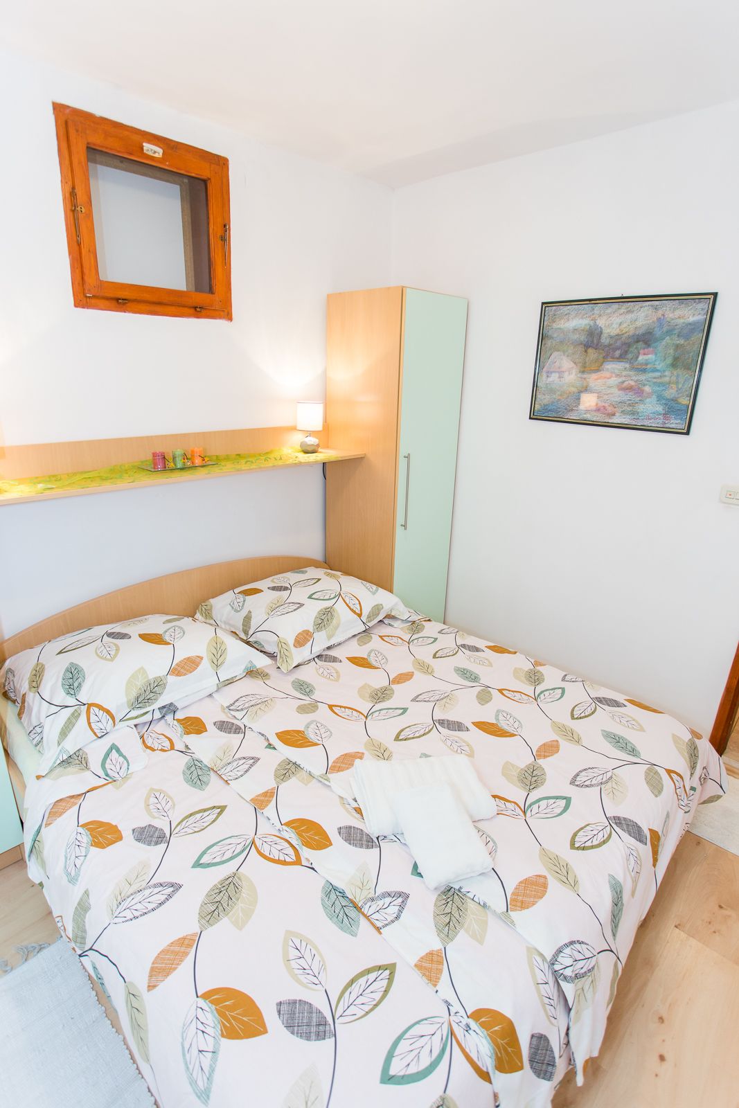 Ein Schlafzimmer mit Bett, Kleiderschrank, Ablagefläche mit Dekoration, Spiegel und einem Bild an der Wand.