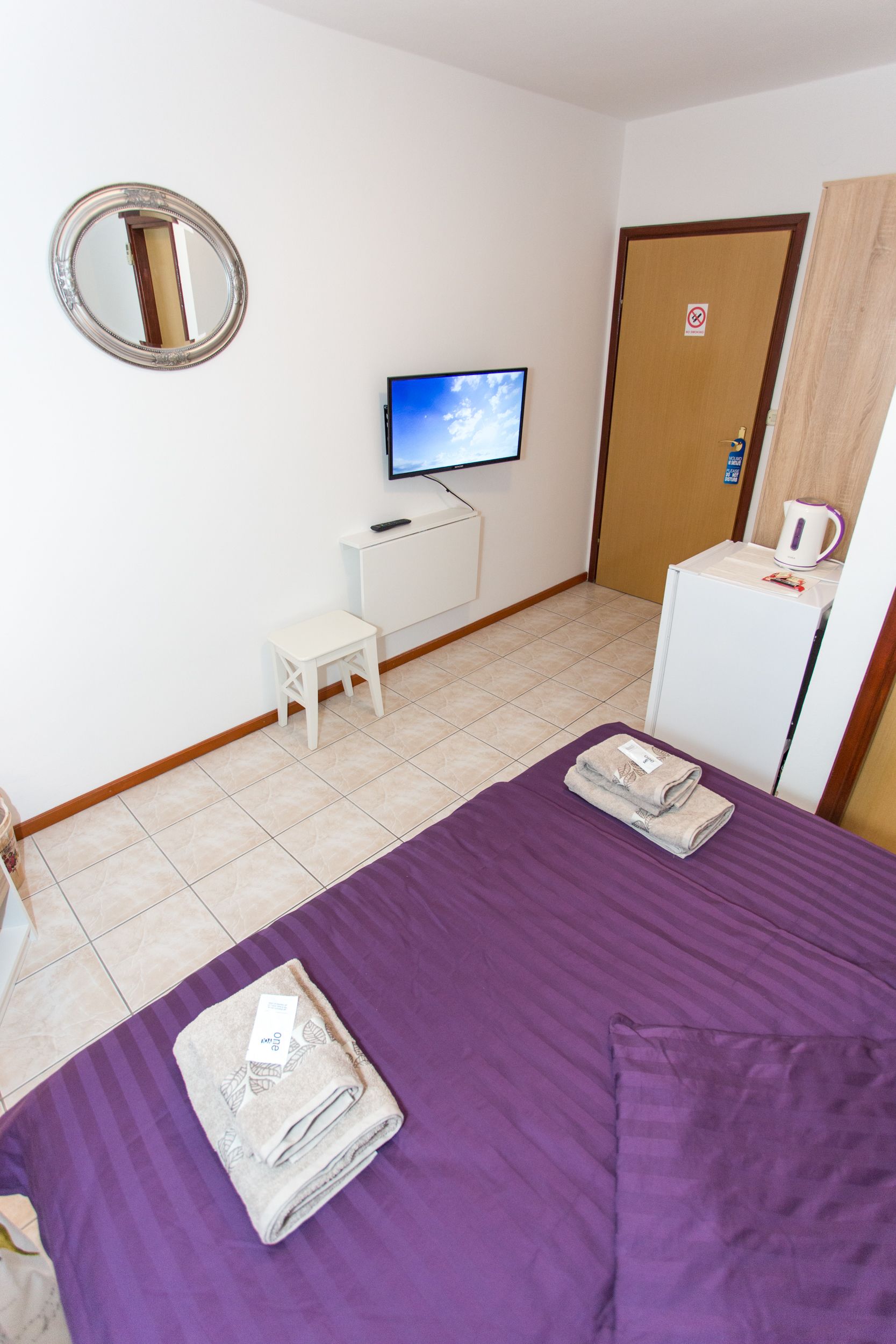 A hotel room with a bed, a television, a small table, and a refrigerator.