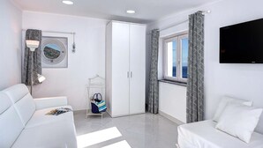 A modern hotel room with a white sofa, a bed, a wardrobe, a TV, and a window with patterned curtains. - Sunrise Suite (Massa Lubrense)