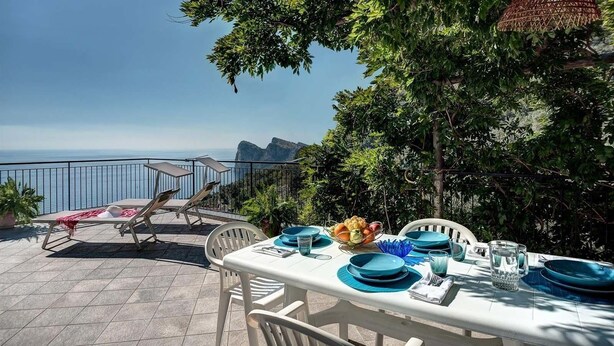An outdoor dining area with a table set for four, overlooking a scenic view of the sea and mountains. - Sunrise Suite (Massa Lubrense)