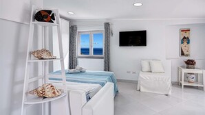 A modern hotel room with a bed, a white sofa, a TV, and a view of the sea. - Sunrise Suite (Massa Lubrense)