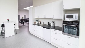 A modern kitchen with white cabinets, a black countertop, a microwave, an oven, and a dishwasher. - Hostel Brønderslev (Bronderslev)