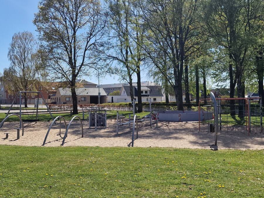 A park with exercise equipment, benches, and trees.