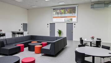 A modern conference room with a large screen, a sectional sofa, round tables, and chairs.
