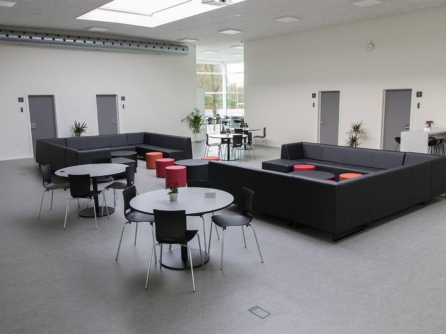 A modern lounge area with black sofas, red ottomans, and round tables.