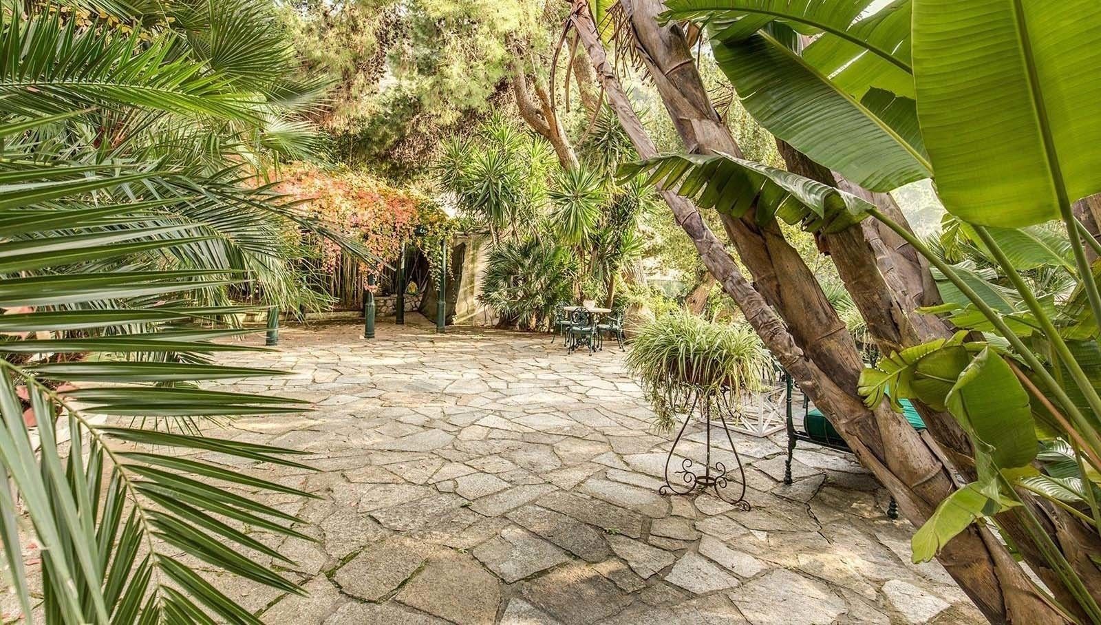 Eine terrasse mit Steinpflaster, tropischen Pflanzen, einer rustikalen Holzkonstruktion und Gartenmöbeln.
