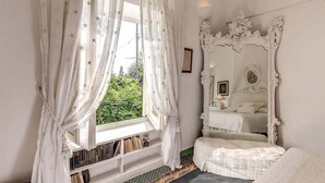 A bedroom with a large ornate mirror, a window with star-patterned curtains, and a bookshelf. - Green Coral (Capri)
