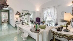 A spacious living room with a white sofa, a coffee table, and a dining area with a white table and chairs. - Green Coral (Capri)