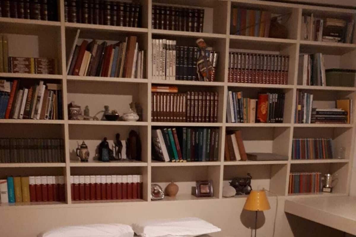 Une chambre à coucher avec un grand lit en bois, une table de chevet avec une lampe et une bibliothèque remplie de livres et d’objets décoratifs.