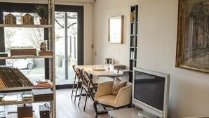 A modern living room with a wooden floor, a TV, a sofa, and a dining area with chairs. - Bed & Breakfast San Lazzaro Room (San Lazzaro di Savena)