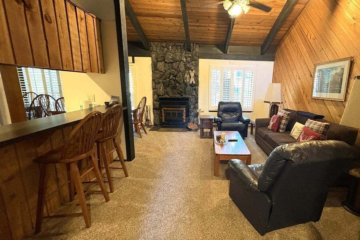 A cozy interior with a stone fireplace, a leather sofa, a dining area with wooden chairs, and a bar area.