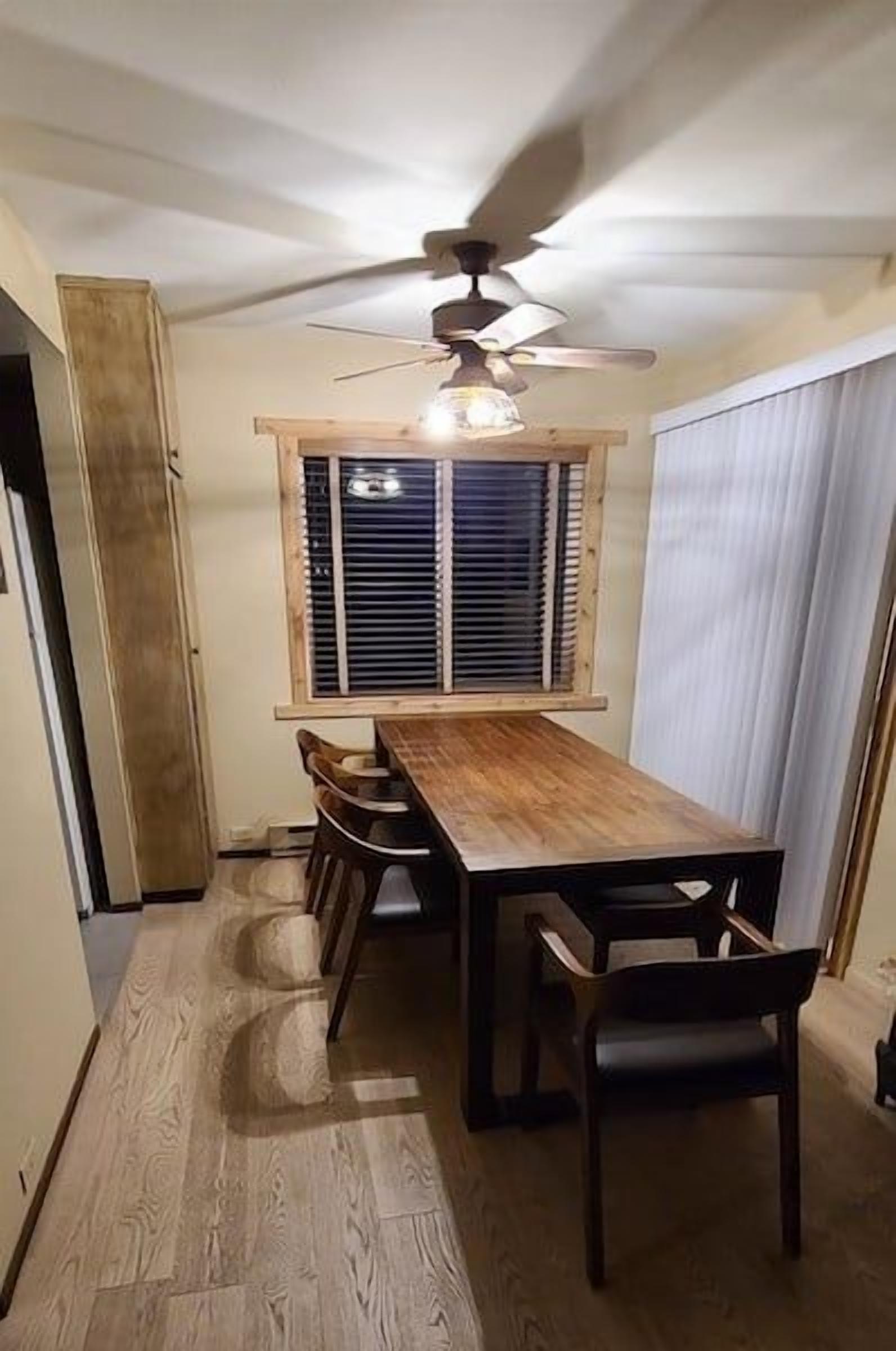 Un comedor con una mesa y sillas de madera, un ventilador de techo y una ventana con persianas.